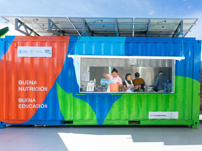 Photo: WFP/Versative/Diego Santamaria Three people inside a brightly coloured container with solar panels and signs promoting nutrition and education.