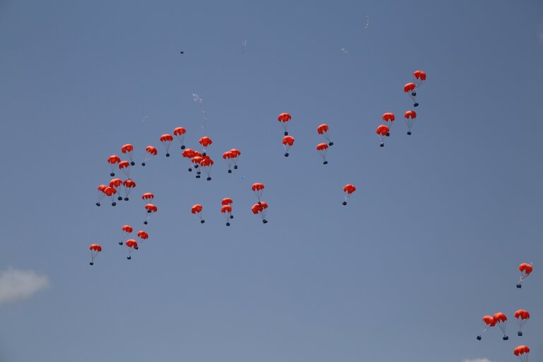 Orange parachutes rain down from a blue sky
