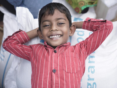 Photo: WFP/Carol Taylor A young smiley boy lays on a rice bag with his hands resting on the back of his head.