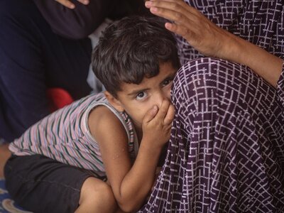 Photo: WFP Child leans on adult in patterned garment; adult's hand rests gently on child's head in a comforting gesture.