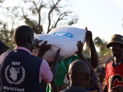 WFP/Nassreen Bachir A WFP staffer is holding a sack of WFP food along with another man whose face is obscured by the sack.