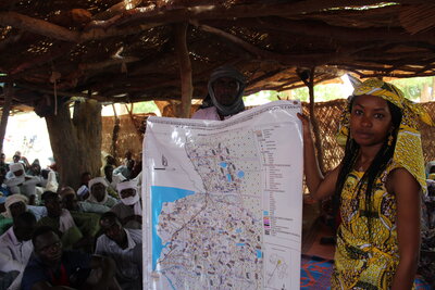 A man holds up a map next to a woman in traditional yellow dress and headdress in Chad