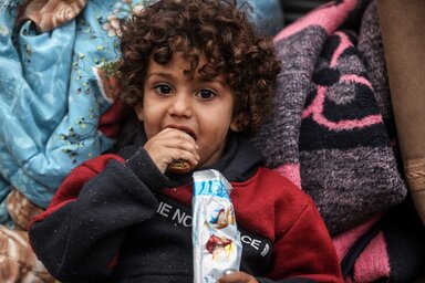 A little child with curly hair eating a biscuit provided by WFP.