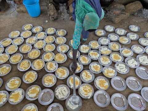 A women leans towards there ground to fill one of dozens of plates set out on a kitchen floor