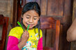 An Indigenous young girl in a pink and yello long-sleeved shirtsmiles as she eats leafy vegetables