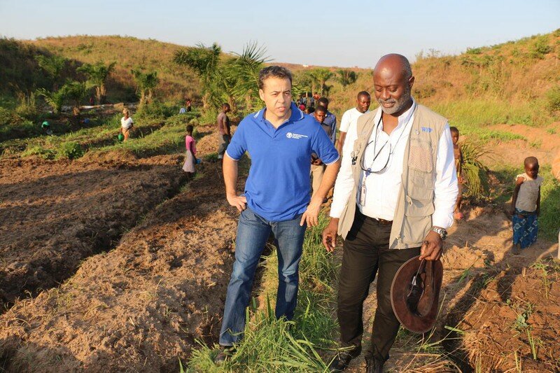 Two man in FAO and WFP gear respectively standing in a field