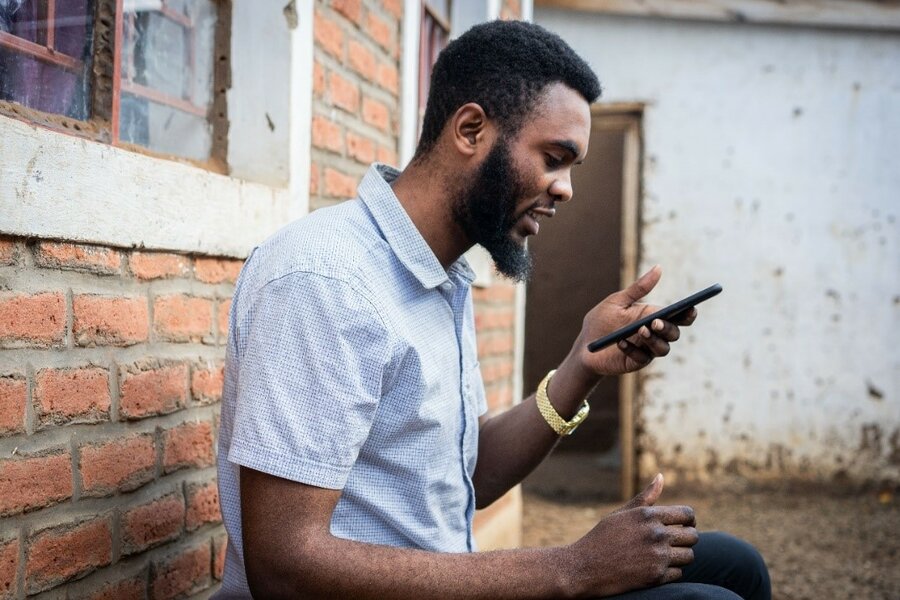 A man sits near a brick wall while looking down at a phone in his hand.