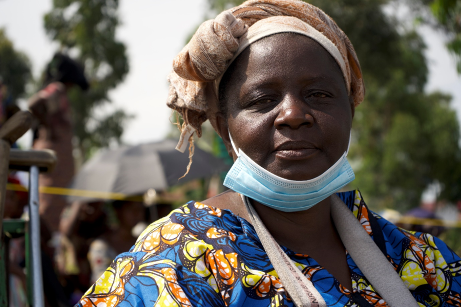 A women wears a disposable blue mask pulled down under her mouth and looks directly into the camera.