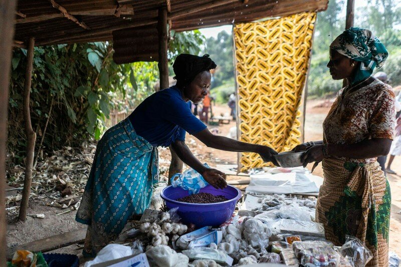 A woman in front of a purple dish hands another woman a smaller dish.