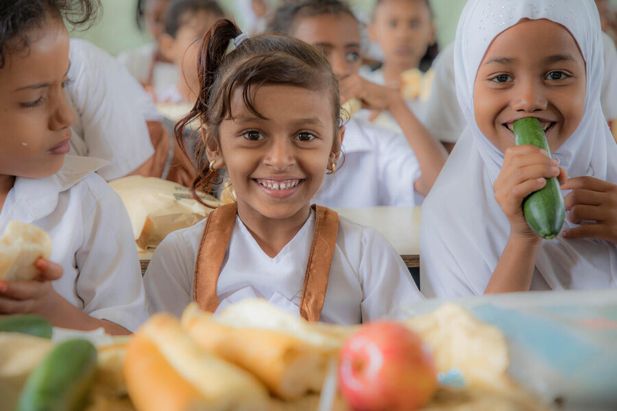 Children sitting down and smiling as they eat food while at school