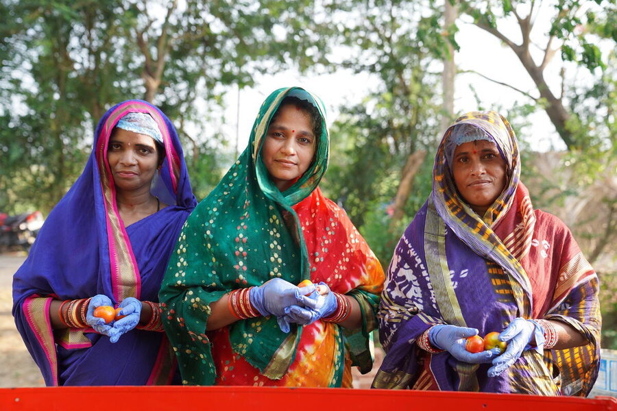 Three women standing and facing camera holding fruit