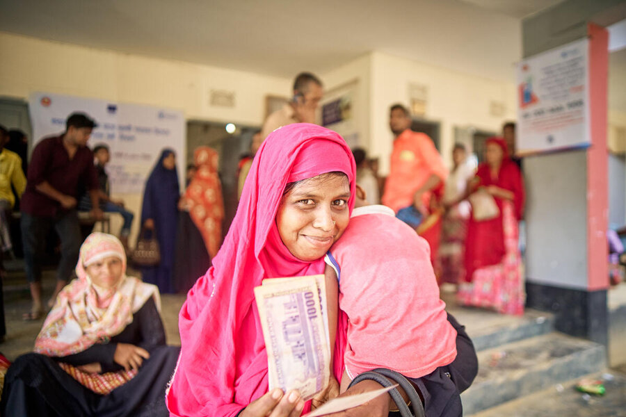 A woman holding a baby and holding up cash to camera