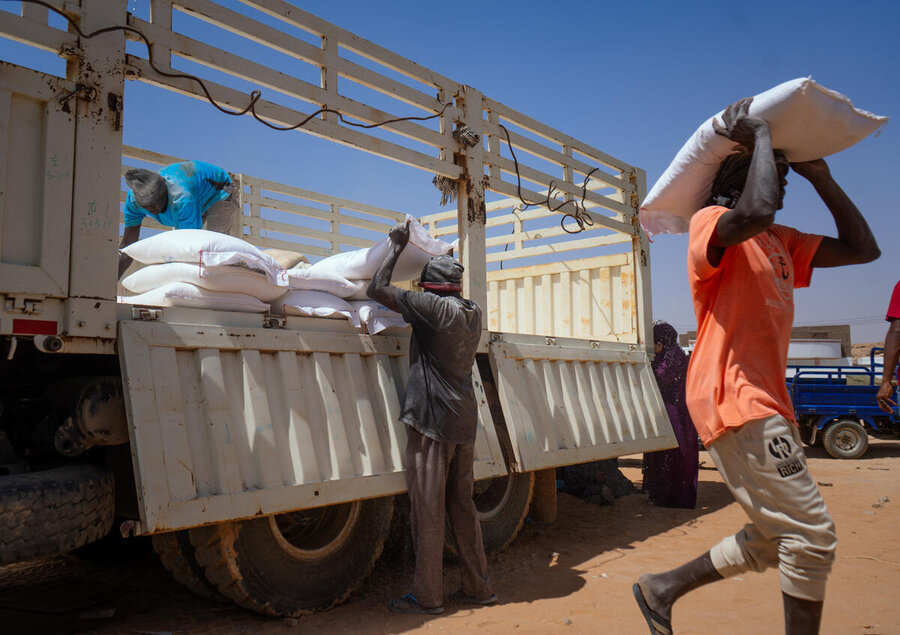 A man carries a bag of wheat flour from a truck