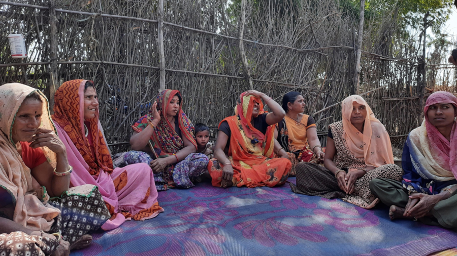 A group of tribal women sits on the floor in a circle in India