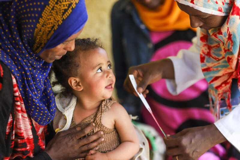 A mother in a purple headscarf holds her baby at a malnutrition clinic in Ethiopia