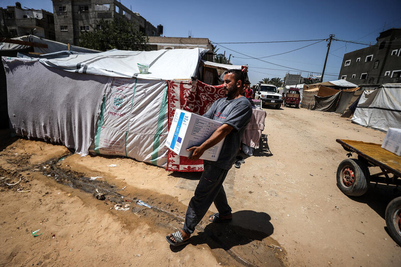 A Palestinian man walks among makeshift tents carrying a box of WFP food