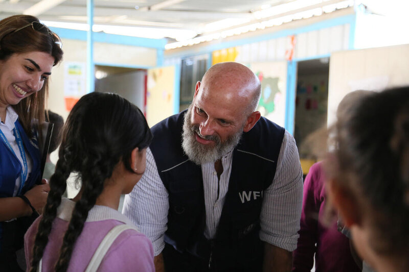 a bearded man in navy blue WFP vest smiles as he talks to a girl with plaits