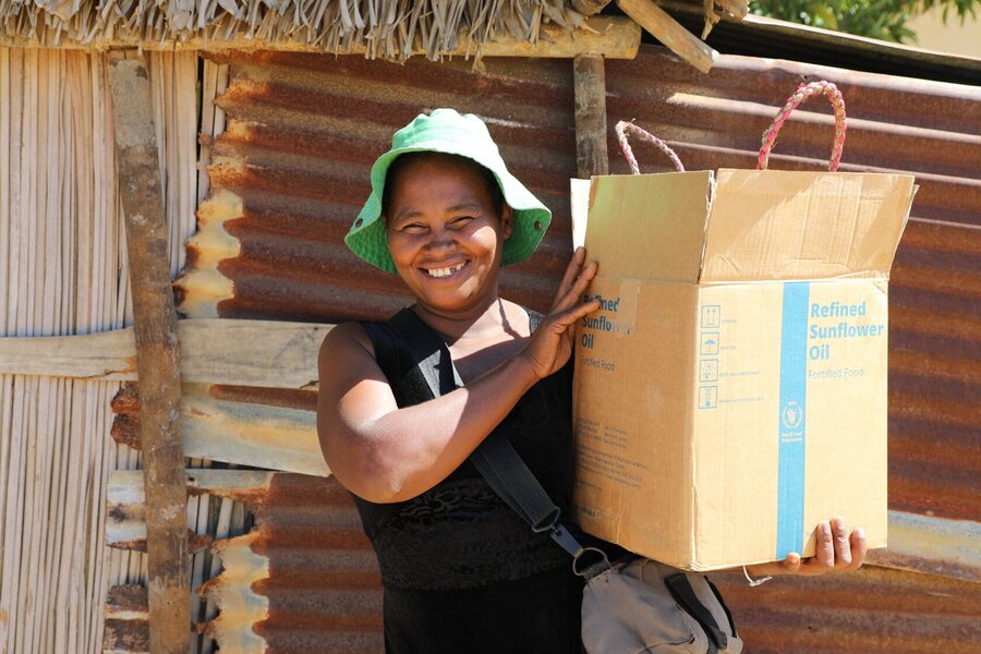 A woman wearing a green sun hat smiles as she holds a brown box with a WFP blue stripe