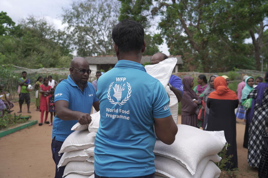  A man, his back turned, in a blue WFP logo shirt unpacks sacks alongside a colleague, in a village