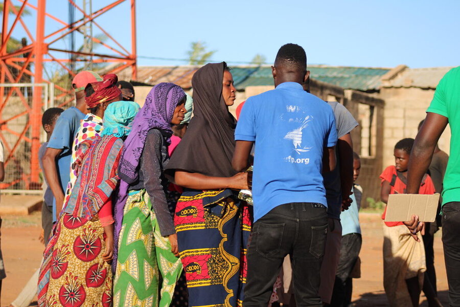 Man with blue WFP shirt, back to camera, addresses women lining up in colourful dresses