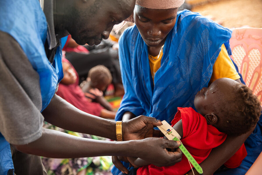 A male medic measures the upper arm of an infant held by a woman