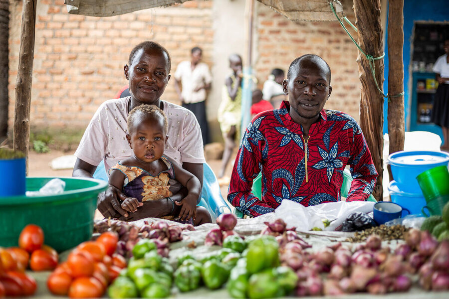 A man and a woman with their infant sat at their vegetables stall