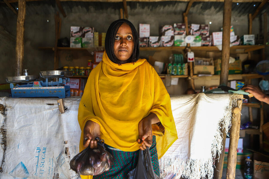 A woman wearing a mustard shawl with a small bag of vegetables at camp shop