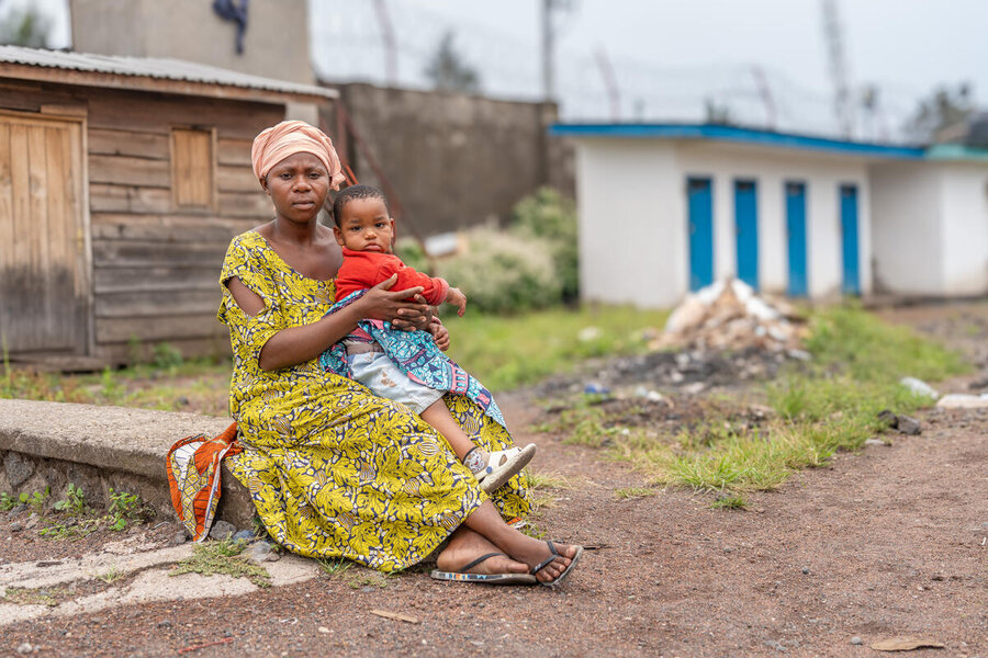 A woman in a green dress with a small child on her lap on a step in a camp