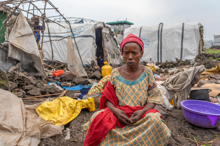 A woman sits in front of partially uncovered tarpaulin tent structures in a displacement camp