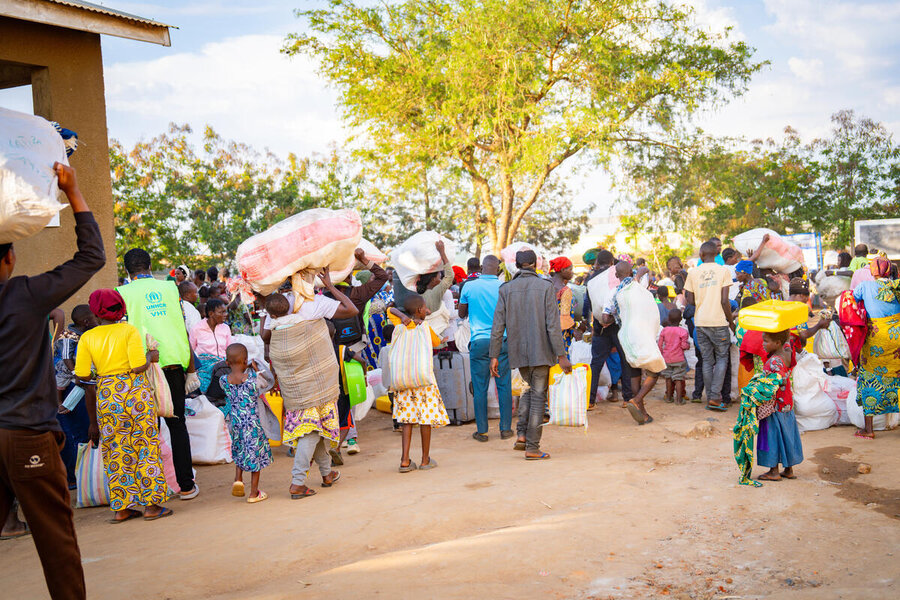 A procession of people carrying belongings arrives at a refugee transit centre in Uganda