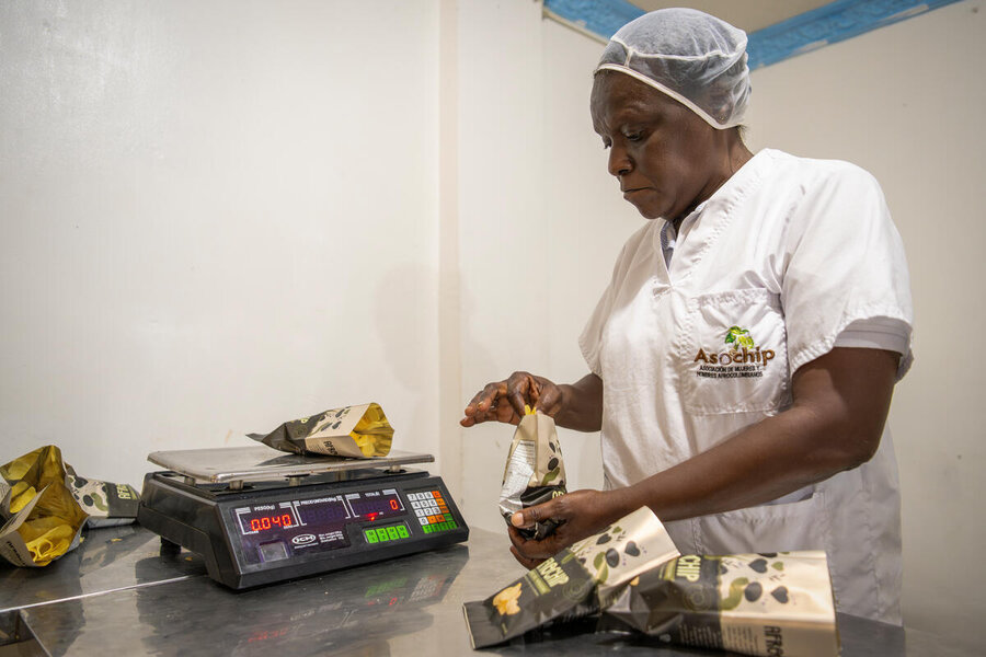 A woman in a white t-shirt wearing a hygiene head net weighs packs of chips