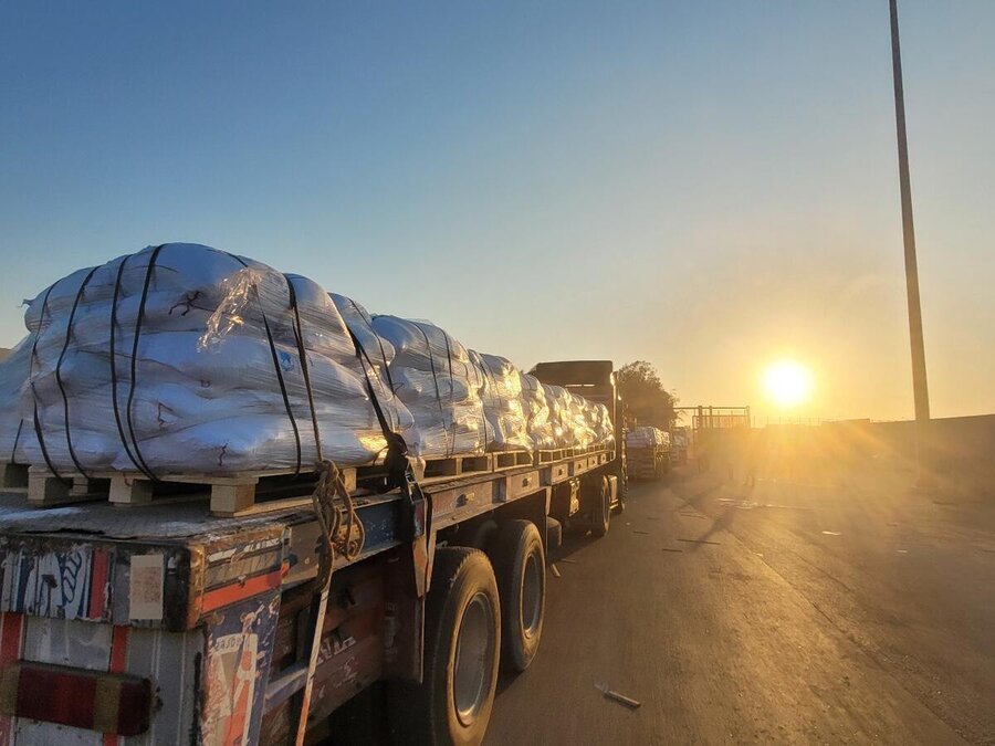 A truck loaded with sacks drives down a road at sunset, casting long shadows.