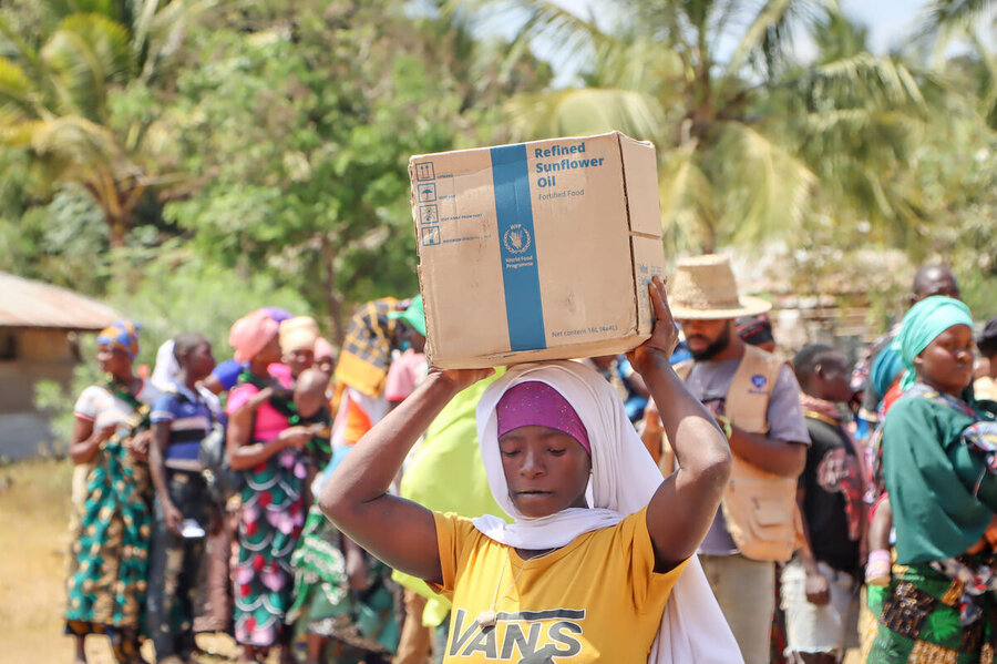 A person balances a box labelled “Refined Sunflower Oil” on their head among a crowd.
