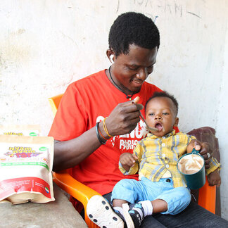 A man is feeding his child with nutritious food provided by WFP