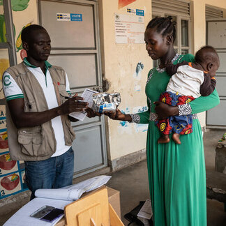 A mom, holding her baby in her arm, is receiving food from WFP staff 