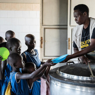 A woman is serving food to the school children