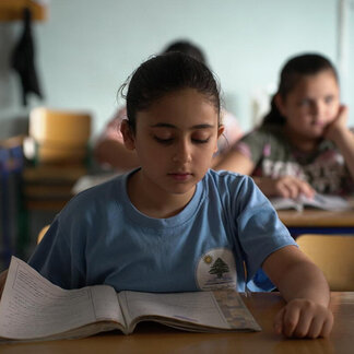 A schoolgirl is reading her book in the class