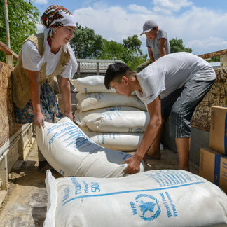 A woman and a man are carrying a WFP food aid sack from a truck